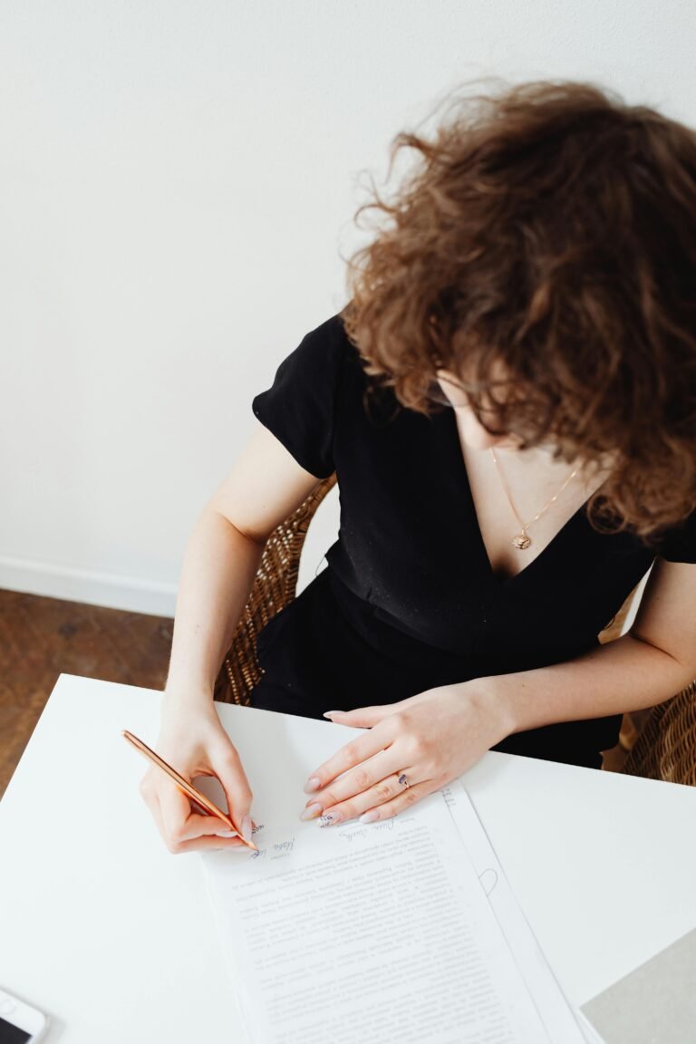 A woman with curly hair signing official documents at a workplace.